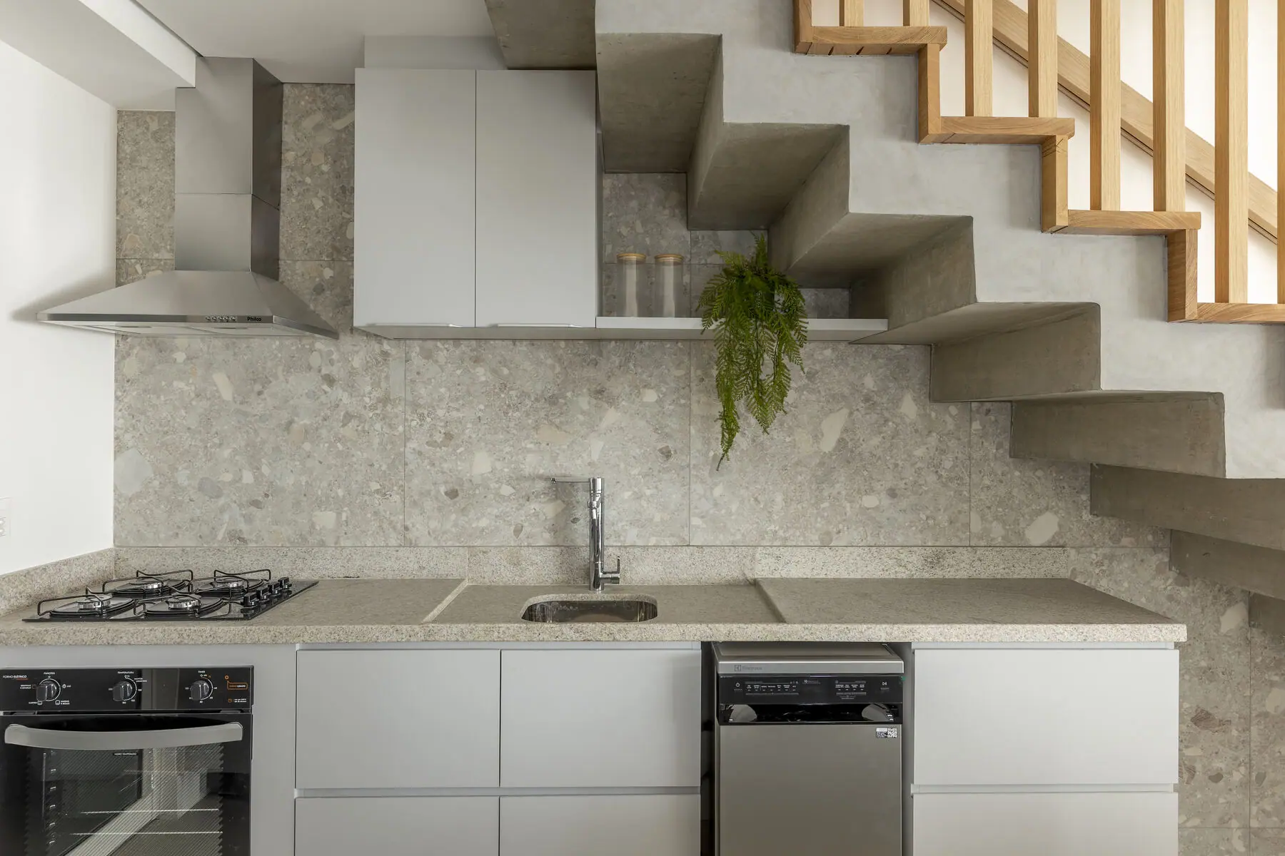 Cozinha com bancada em pedra, cooktop e escada em concreto