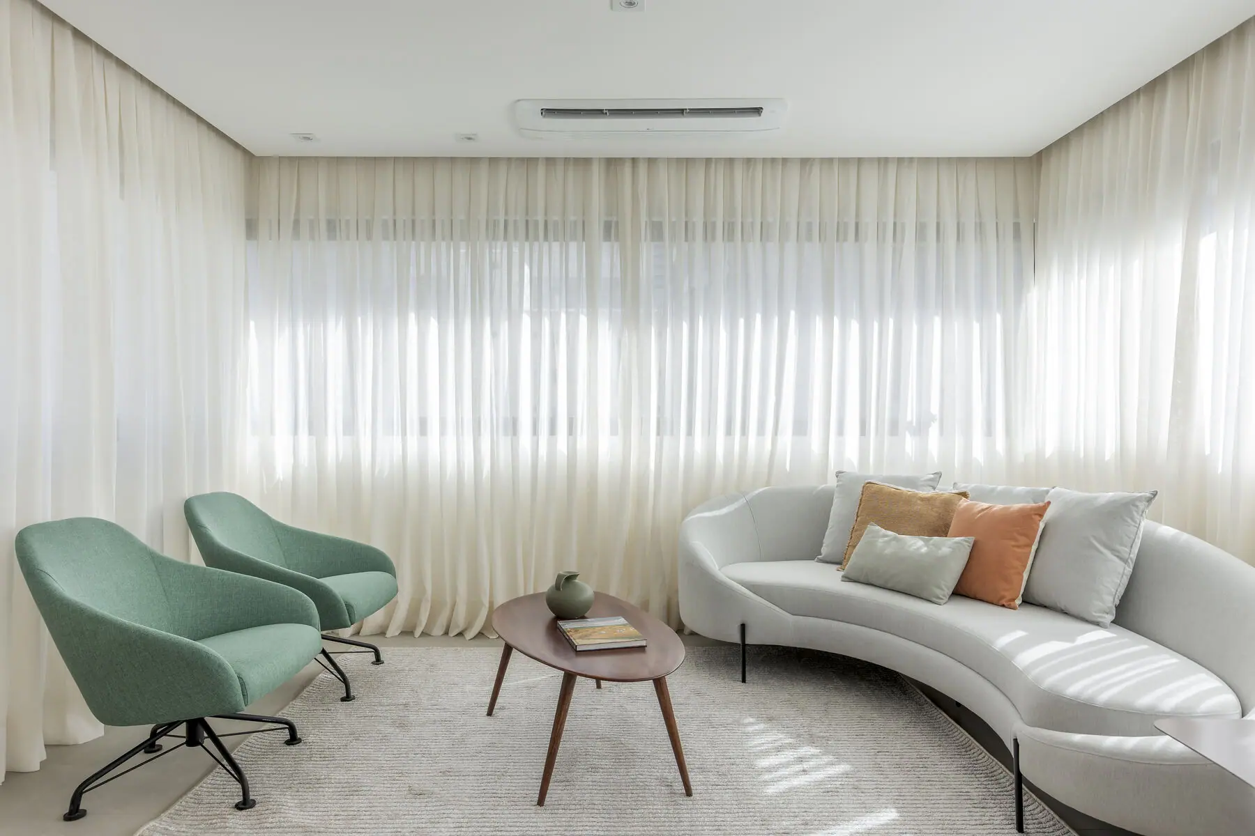 Living com sofá curvo, poltronas e cortinas em voil
